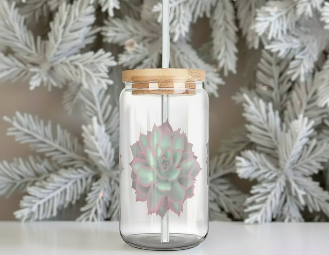Clear glass tumbler with a bamboo lid and straw, featuring a pink succulent design, against a decorative white foliage background.